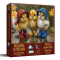 Jigsaw puzzle box featuring three cartoon chicks in raincoats and boots with a scenic background.